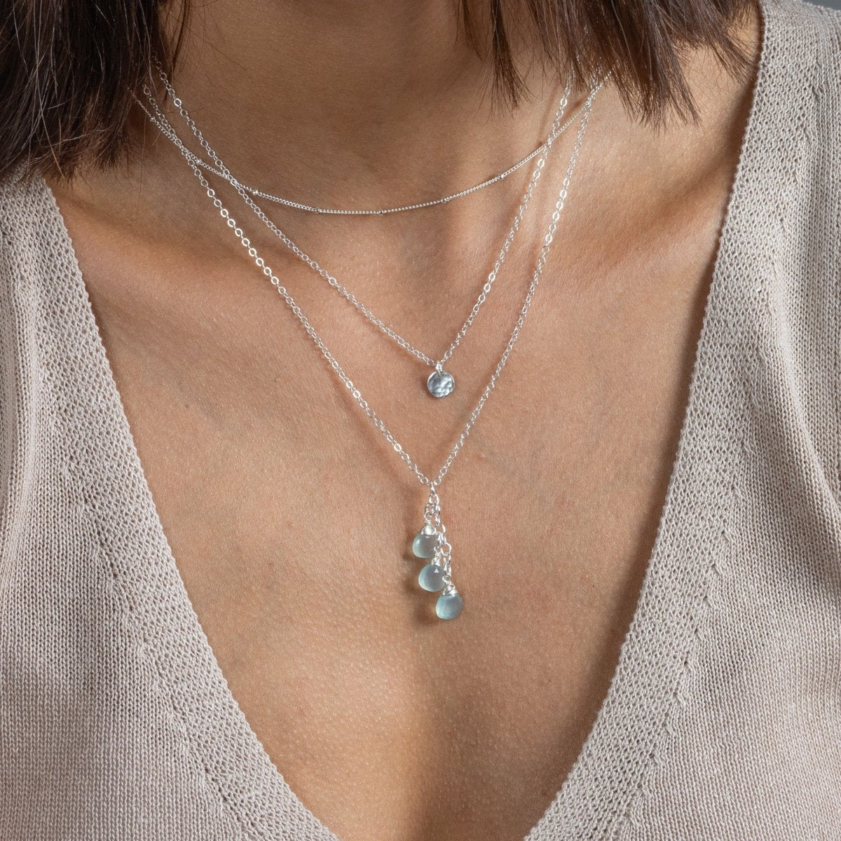 Am Hals des Models sind drei unterschiedlich lange Silberketten angebracht. An der untersten hängen drei hellblaue Edelsteine.