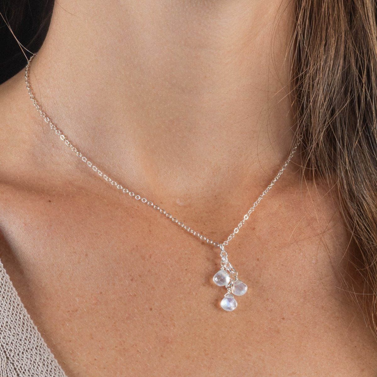 Eine dünne Silberkette mit drei untereinander angebrachten Mondstein-Tropfen hängt am Hals des Models.
