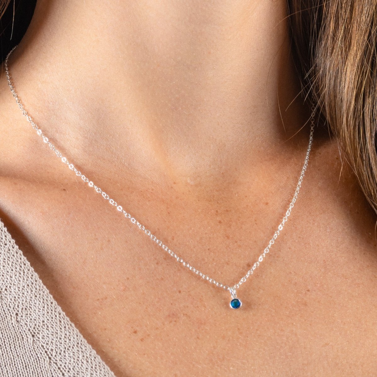 Am Hals des Models hängt eine dünne Silberkette mit einem winzigen, in Silber gefassten, blauen Stein.