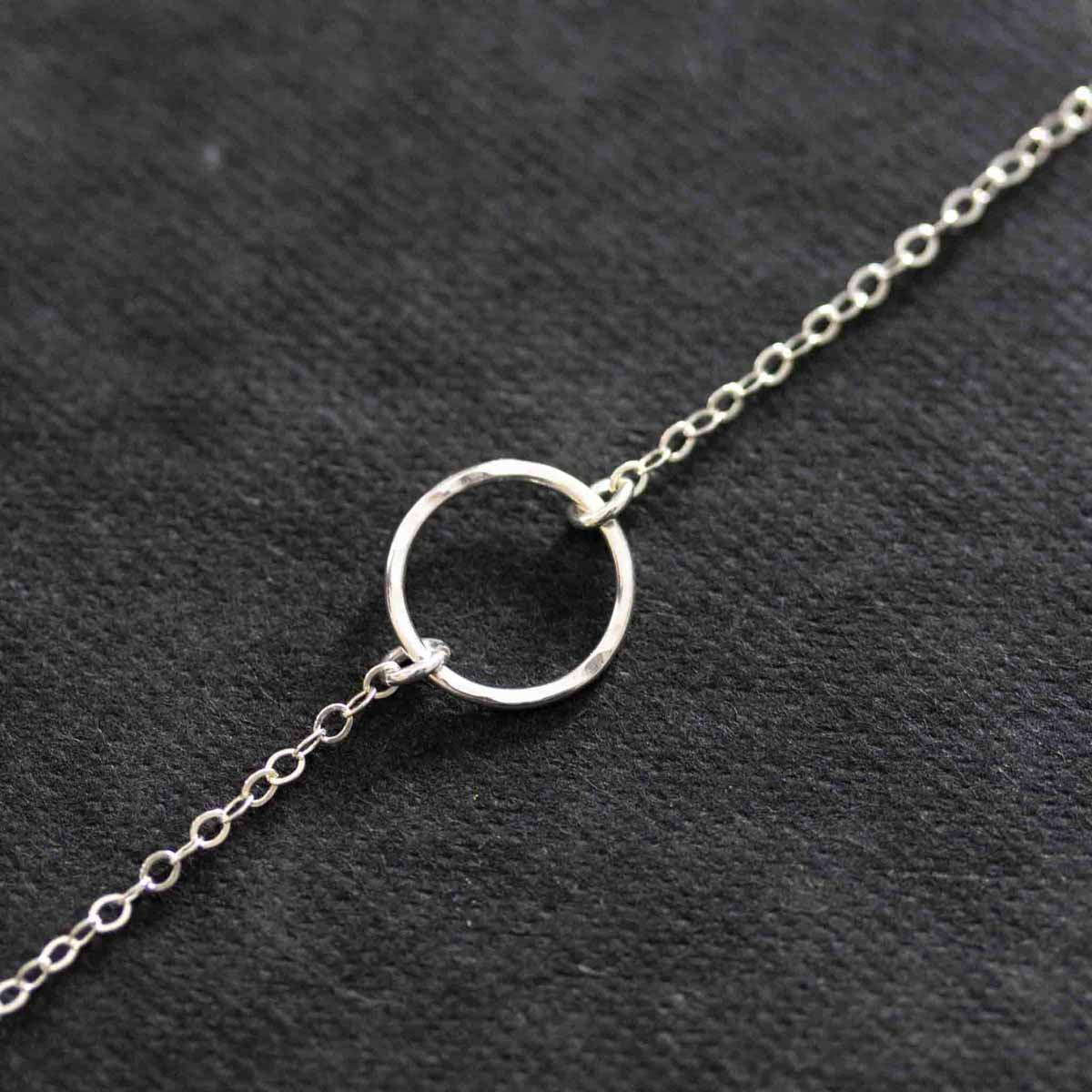 Eine Halskette aus 925 Silber mit einem offenen, gehämmerten Ring als Verbinder auf dunklem Hintergrund.