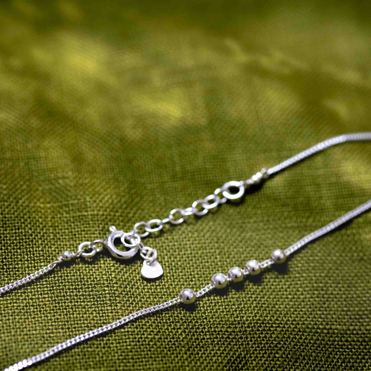 Eine feine 925 Sterlingsilber-Kette mit fünf kleinen silbernen Perlen auf grünem Hintergrund.