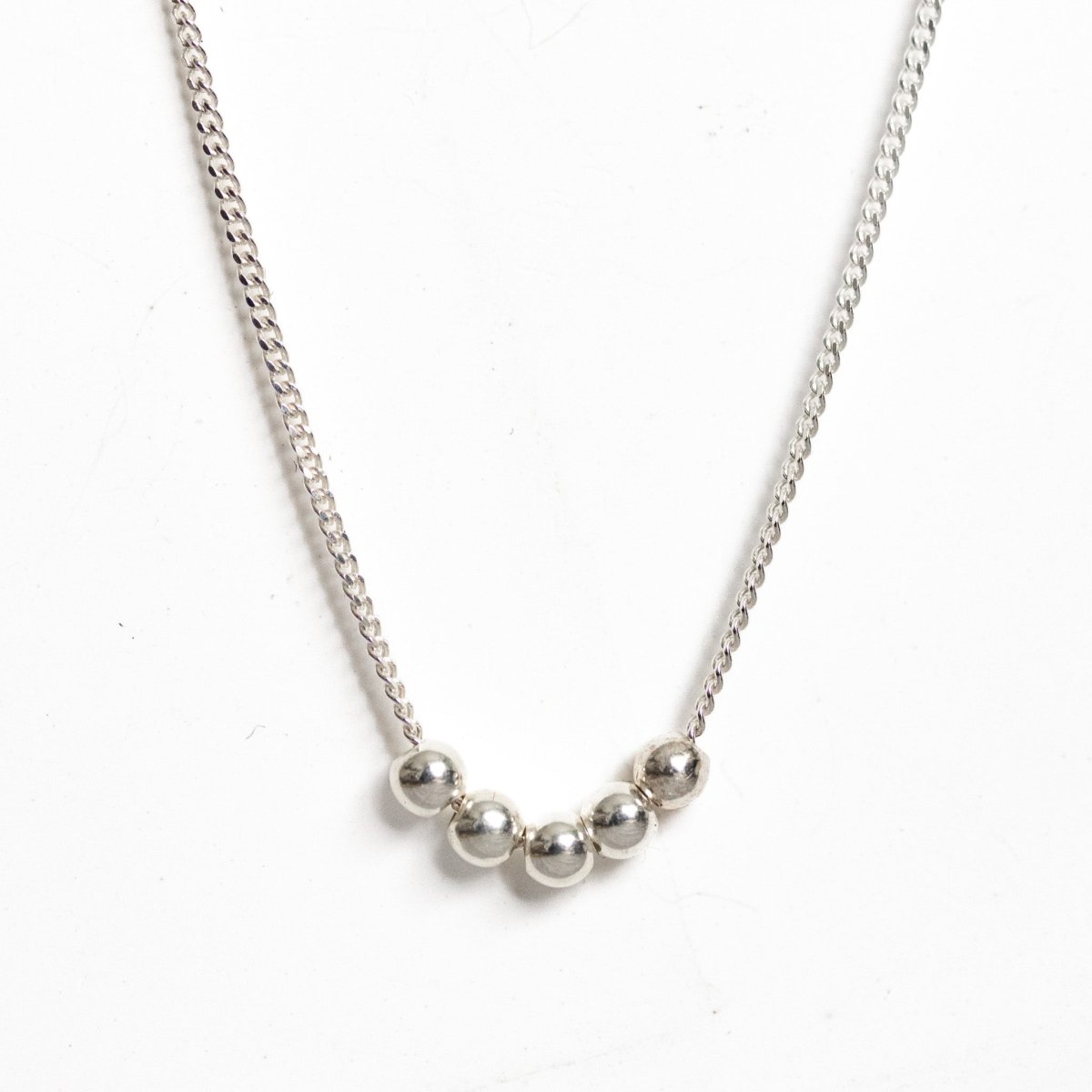 Eine feine Silberkette mit fünf aufgezogenen, kleinen Silberperlen hängt vor einem weißen Hintergrund.