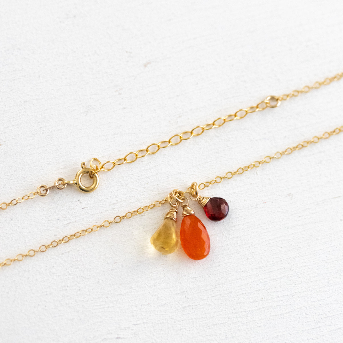 Zierliche Goldkette mit Citrin-, Karneol- und Granat-Anhänger vor weißem Hintergrund gehängt. Detailansicht mit Federring-Verschluss und Verlängerungskettchen.