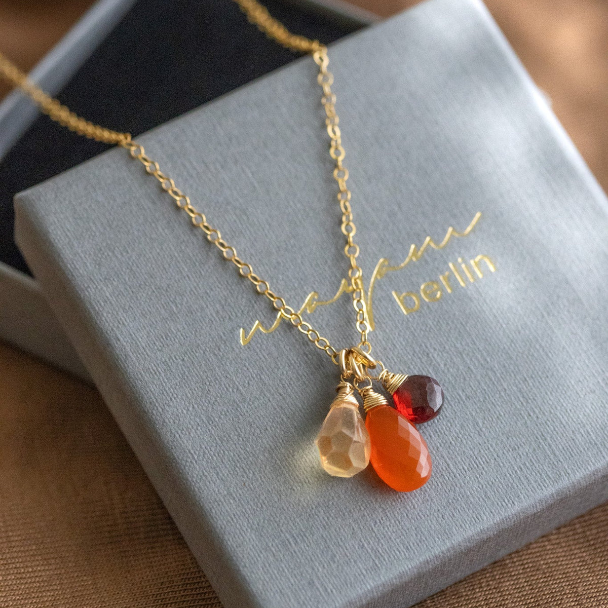 Zierliche Goldkette mit Citrin-, Karneol- und Granat-Anhänger auf Deckel eines Etuis ausgelegt.