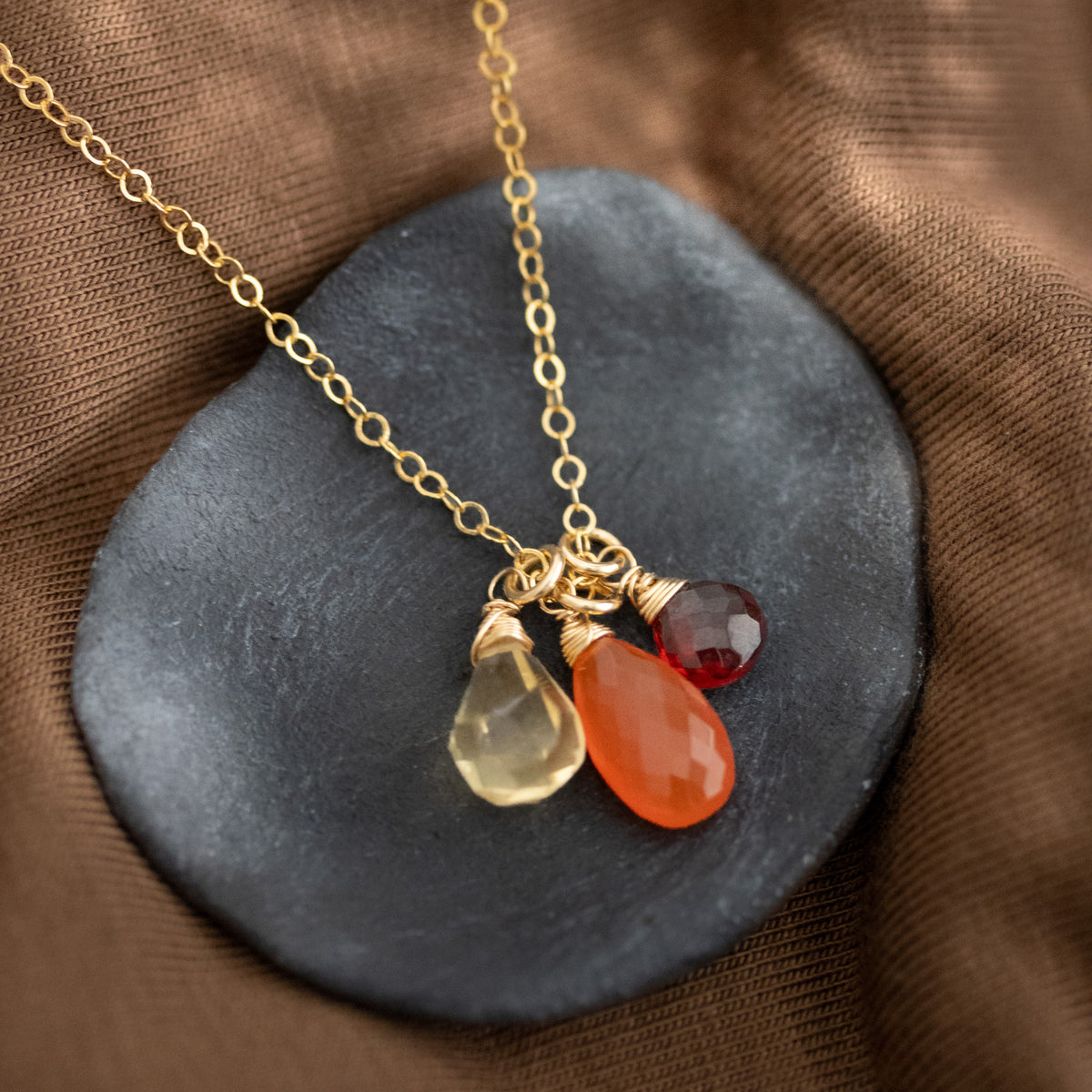 Zierliche Goldkette mit Citrin-, Karneol- und Granat-Anhänger auf Schale ausgelegt.