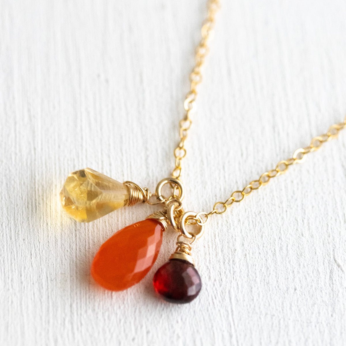 Zierliche Goldkette mit Citrin-, Karneol- und Granat-Anhänger vor weißem Hintergrund gehängt.