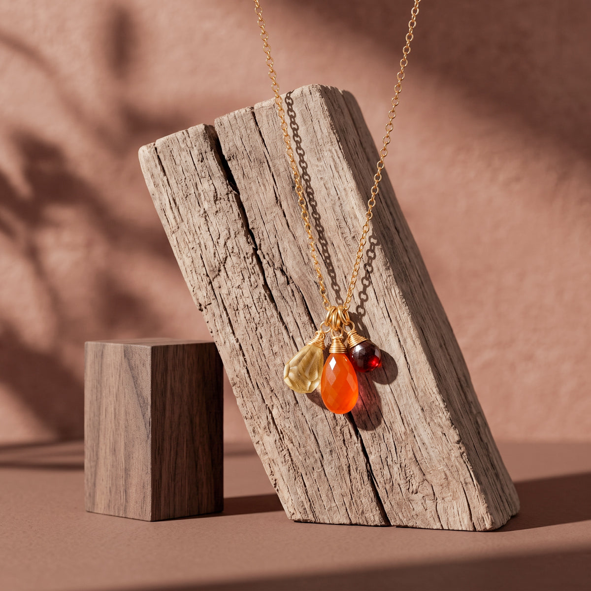 Zierliche Goldkette mit Citrin-, Karneol- und Granat-Anhänger vor Holz hängend.