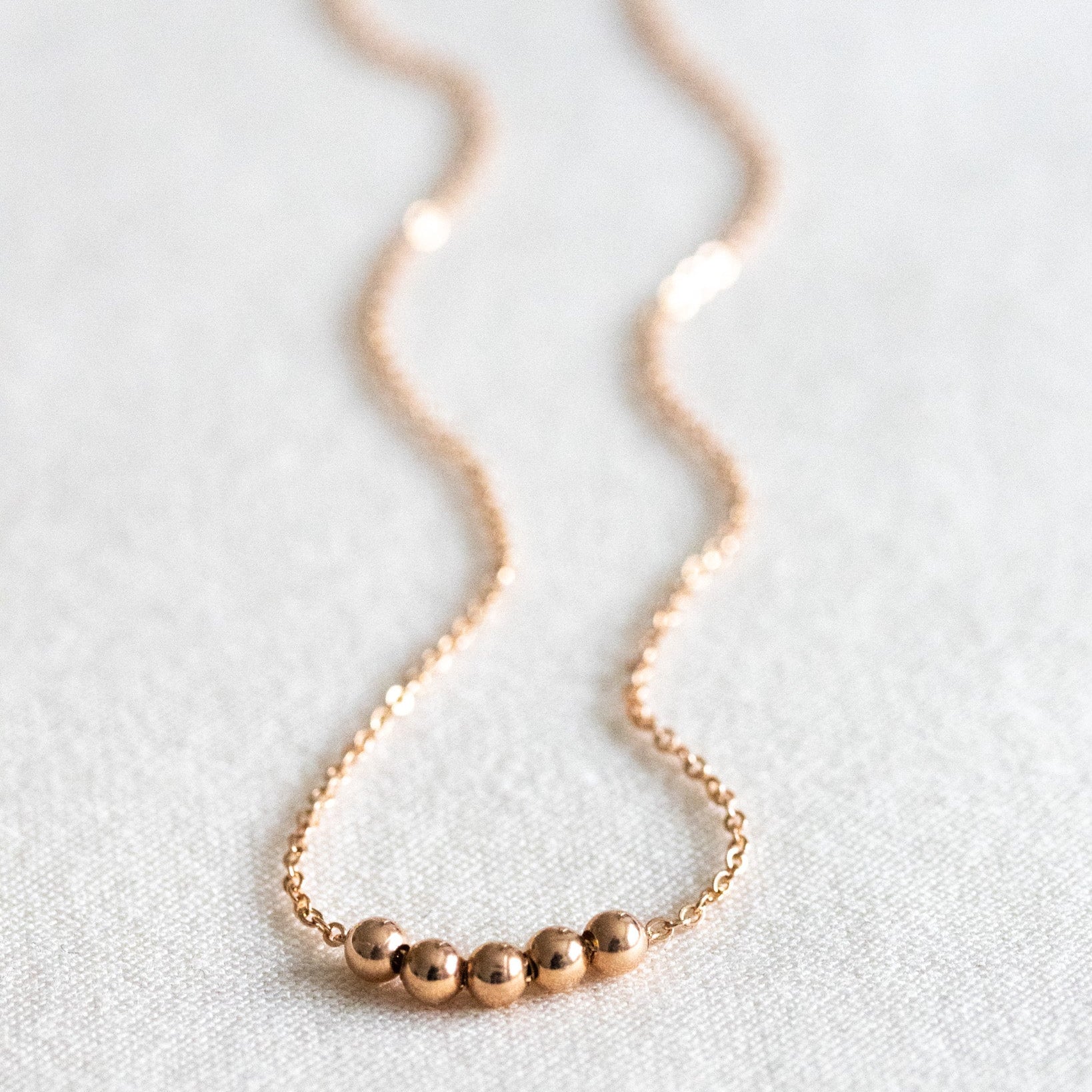 Eine feine Rosé gold-Kette mit fünf kleinen Metallperlen auf weißem Hintergrund.