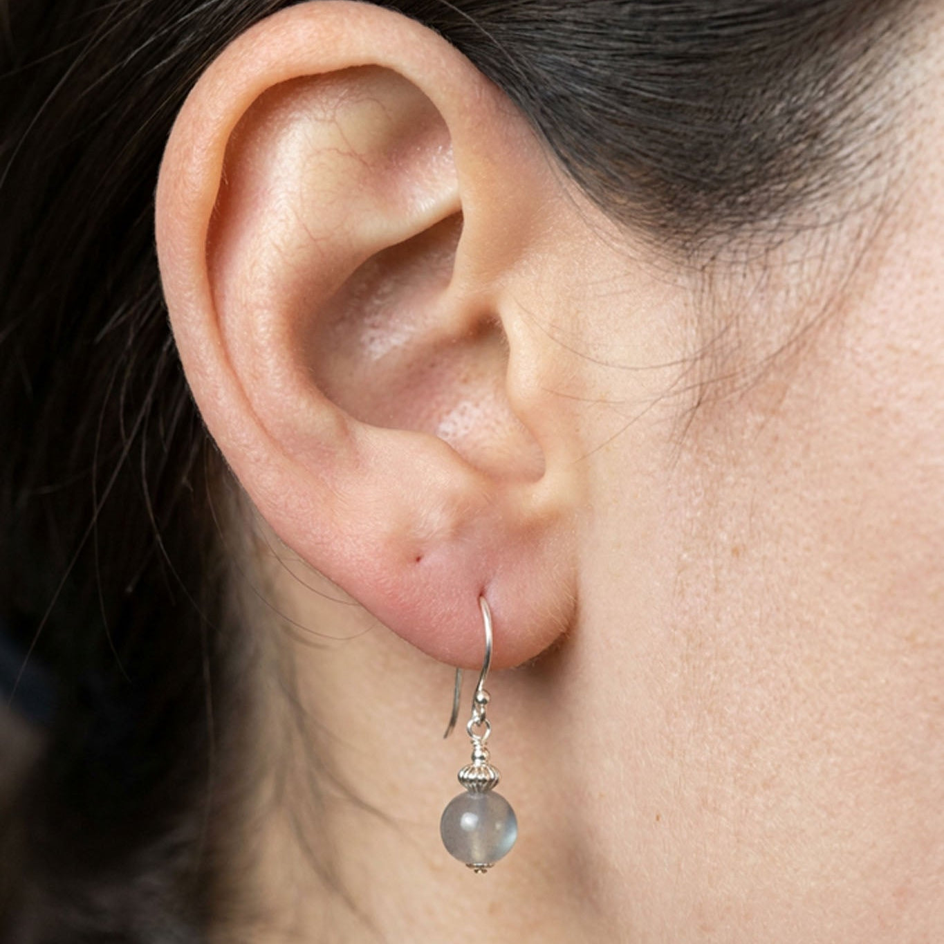 Am Ohr des Models hängt ein Silber-Ohrring mit einer grauen Mondsteinkugel.