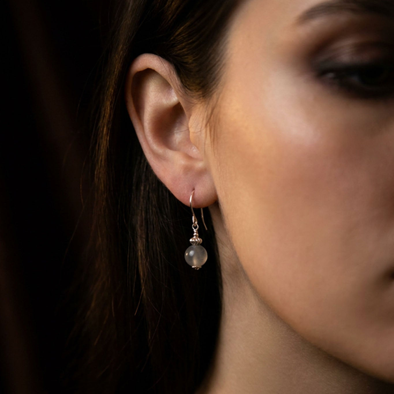 Am Ohr des Models hängt ein Silber-Ohrring mit einer grauen Mondsteinkugel.