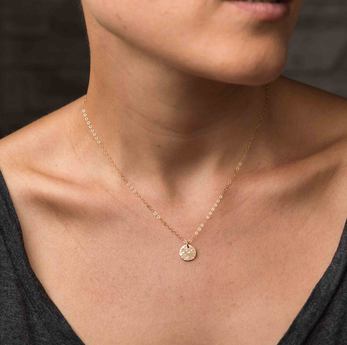 Eine filigrane Goldkette mit gehämmertem, runden Plättchen-Anhänger am Model.