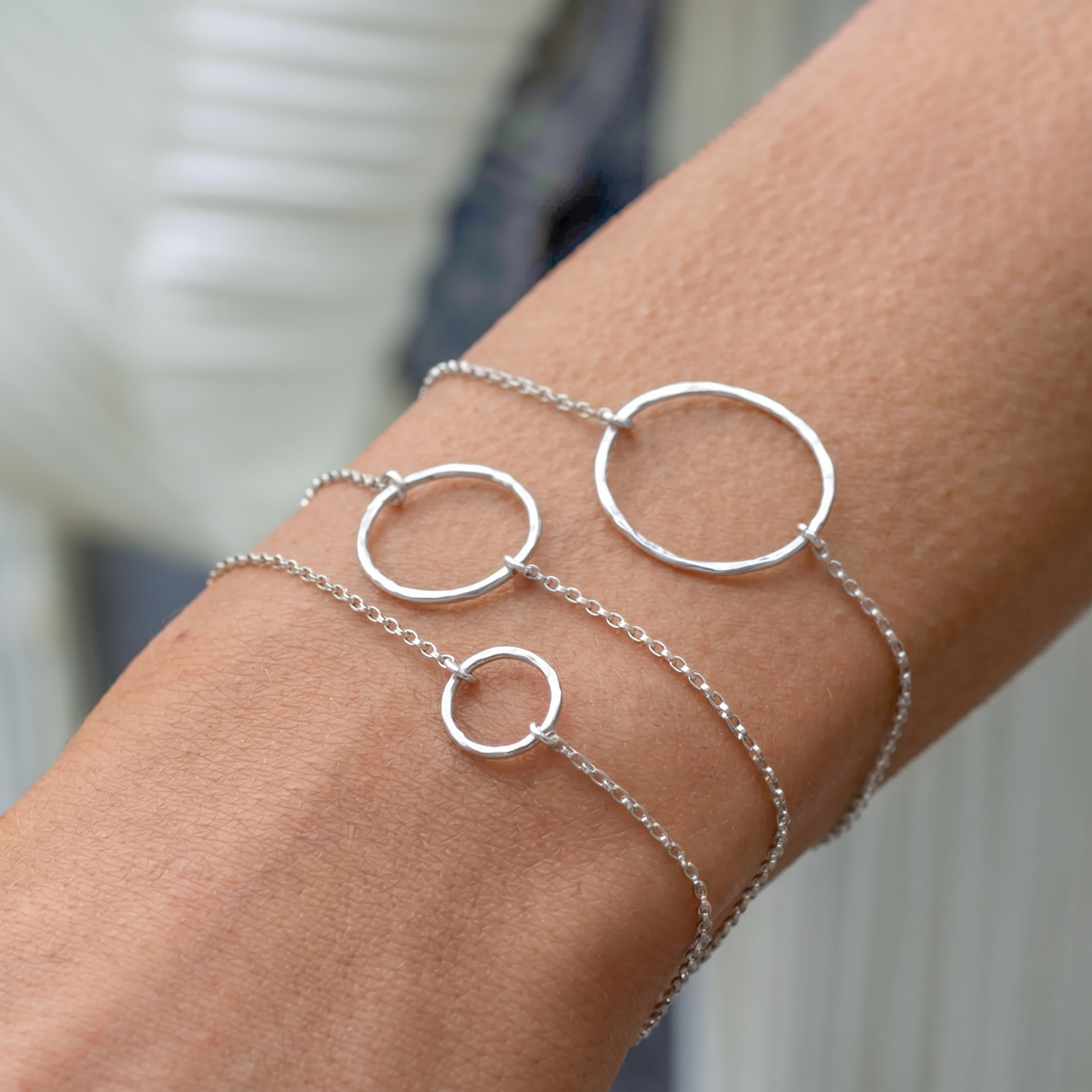 Drei zarte Armbänder aus Sterlingsilber mit gehämmerten Kreisanhängern in drei Größen, übereinander am Handgelenk getragen.