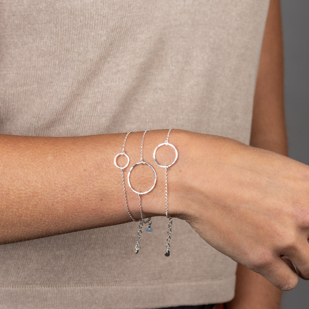 Drei zarte Armbänder aus Sterlingsilber mit gehämmerten Kreisanhängern in drei Größen, übereinander am Handgelenk getragen.