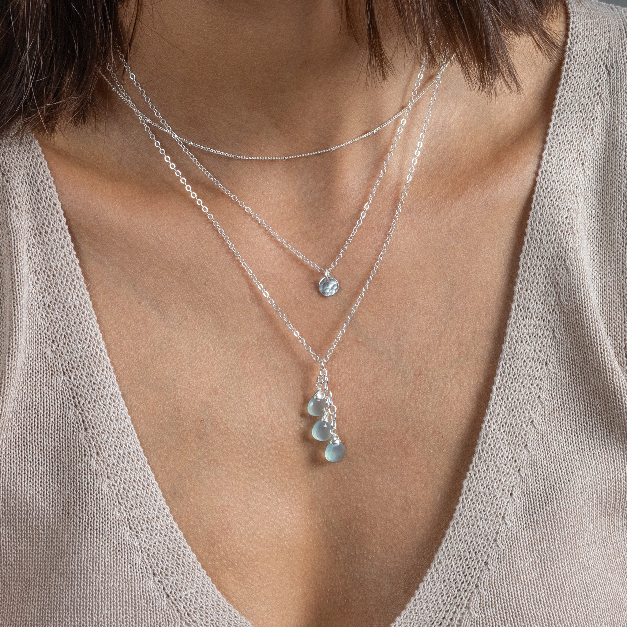 Am Hals des Models sind drei unterschiedlich lange Silberketten angebracht. An der untersten hängen drei hellblaue Edelsteine.