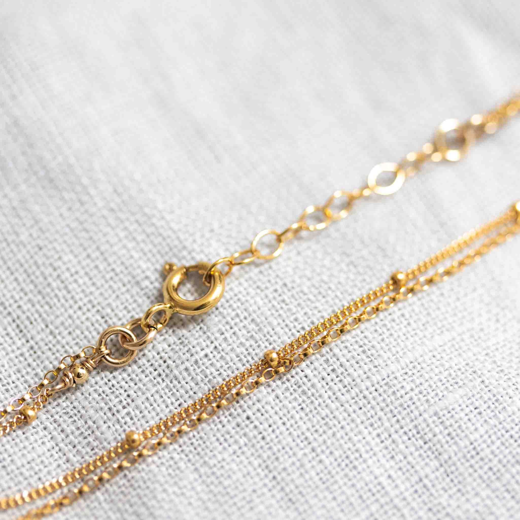 Auf weißem Hintergrund liegt ein zierliches, doppelt gelegtes Armband aus Satellitenkette und Rolokette, beide in gold.