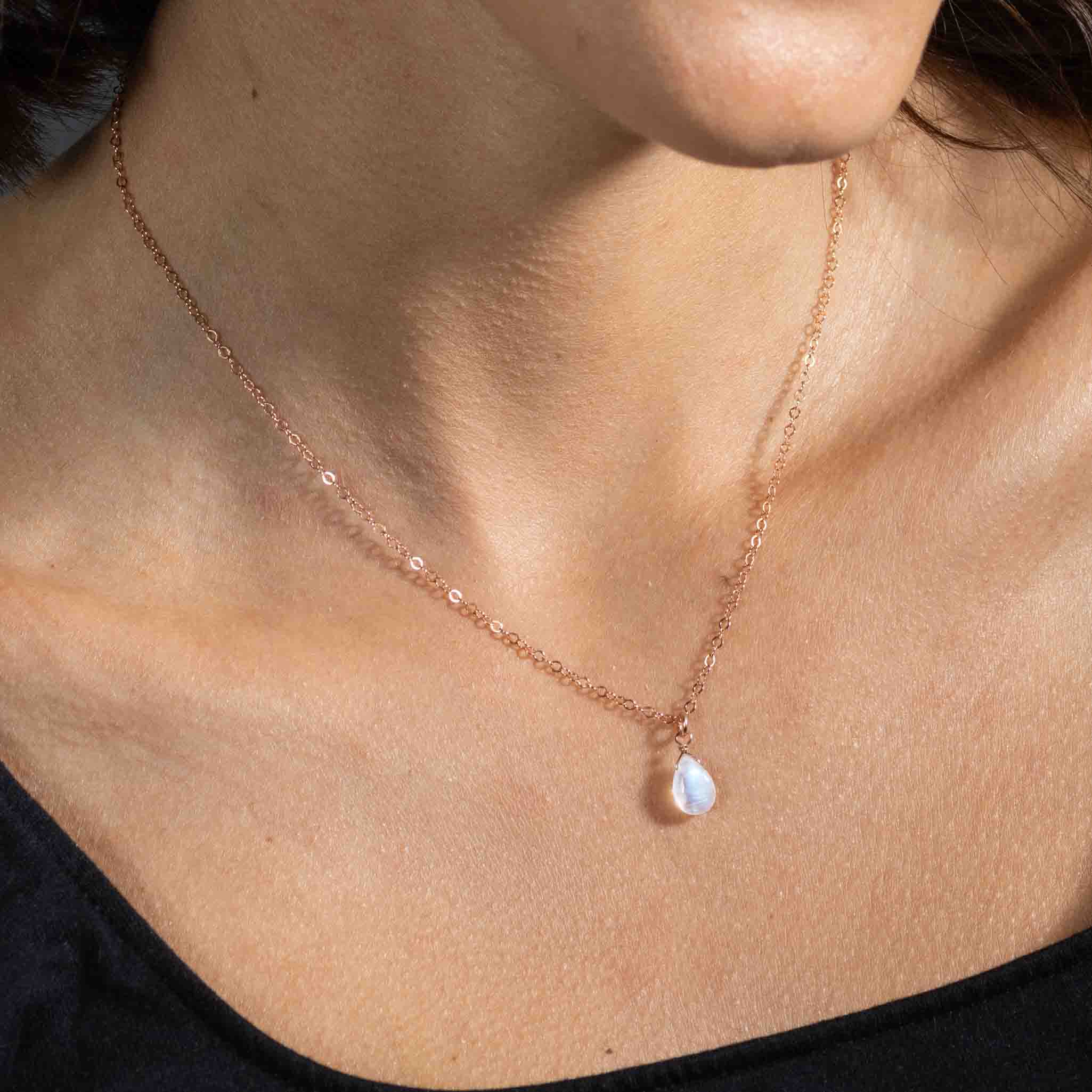Eine feine rosé goldene Halskette mit einem bläulich schimmernden Mondstein-Anhänger hängt am Hals des Models.