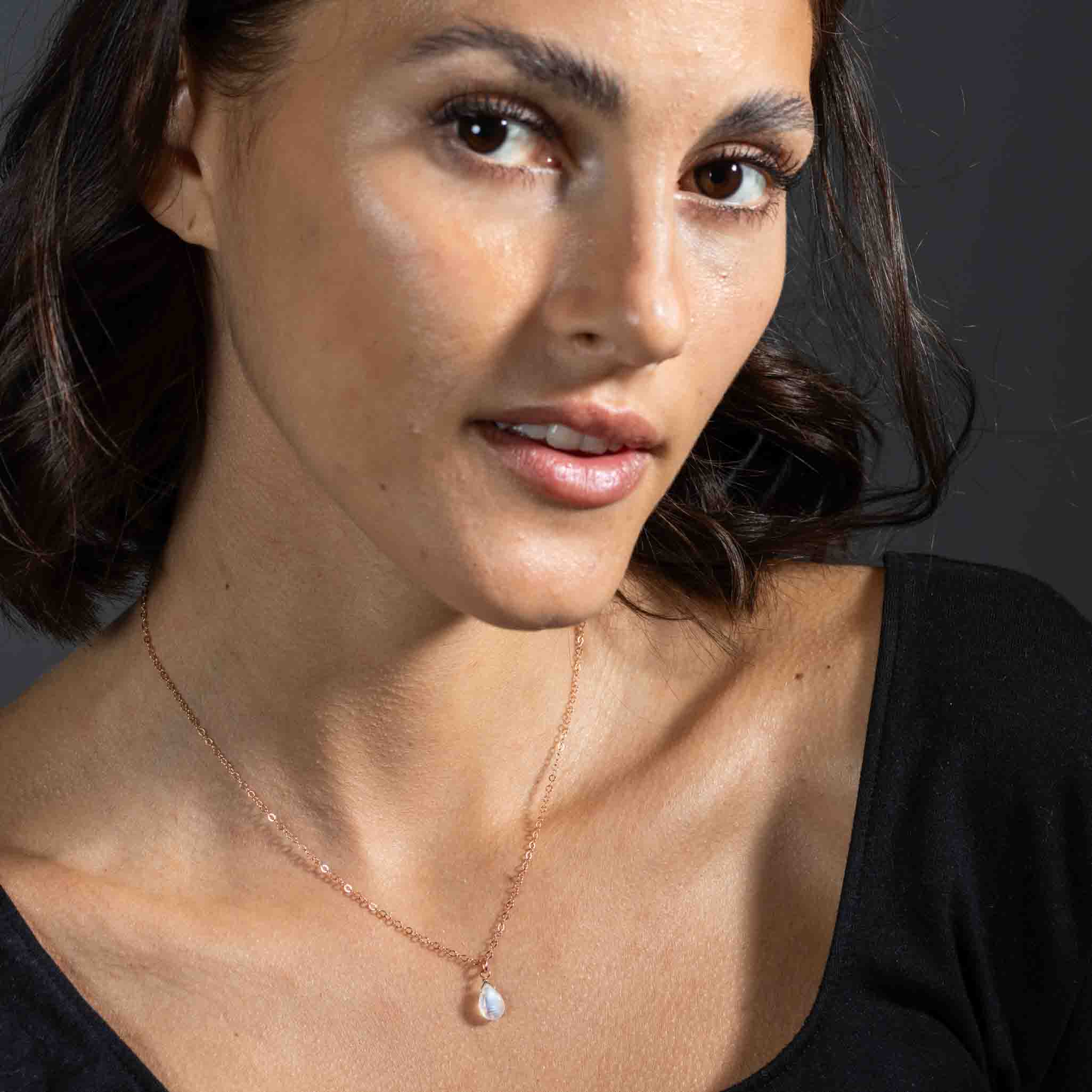Eine feine rosé goldene Halskette mit einem bläulich schimmernden Mondstein-Anhänger hängt am Hals des Models.