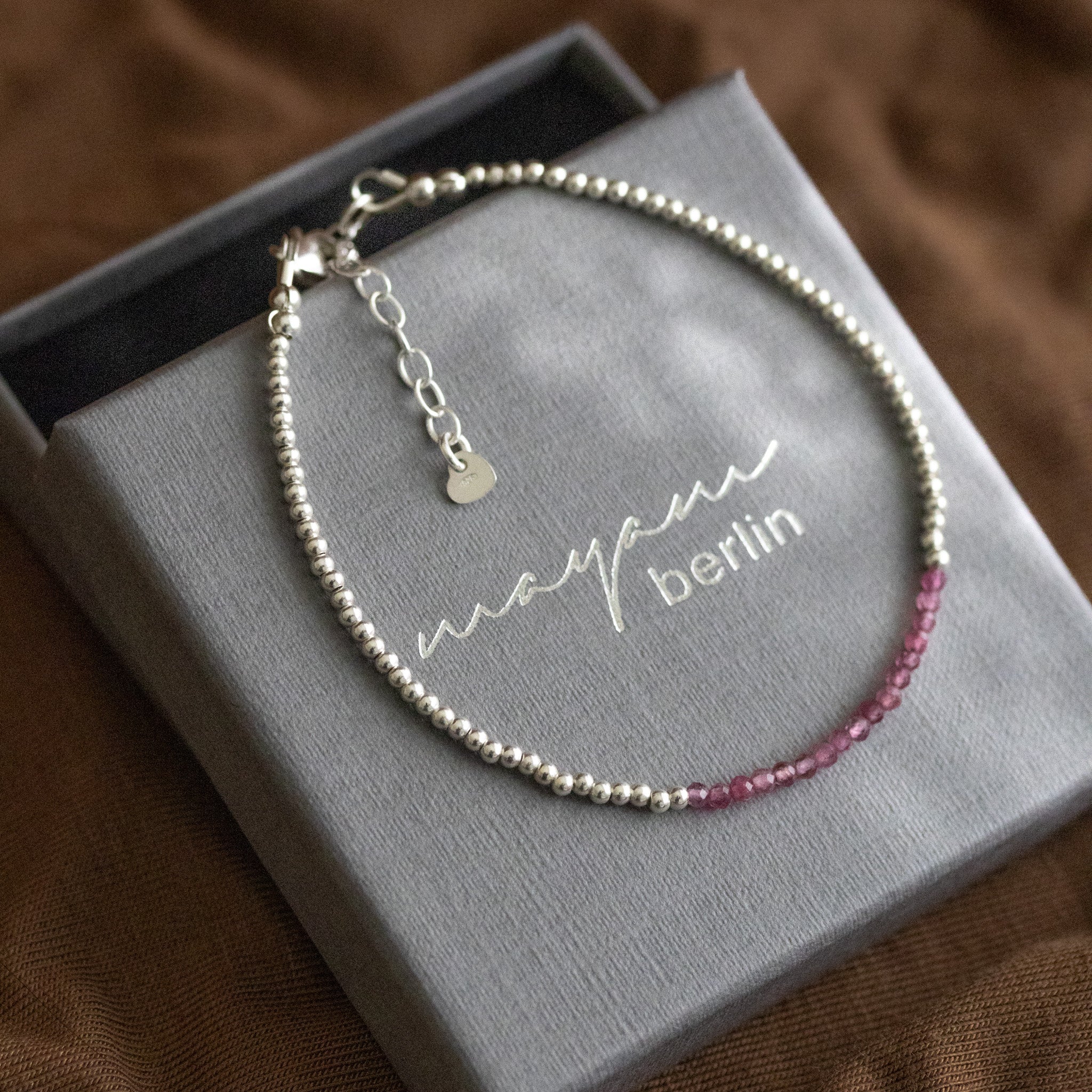 Ein sehr dünnes Silberarmband mit winzigen rosa Turmalinen in der Mitte liegt auf einem grauen Schmucketui.