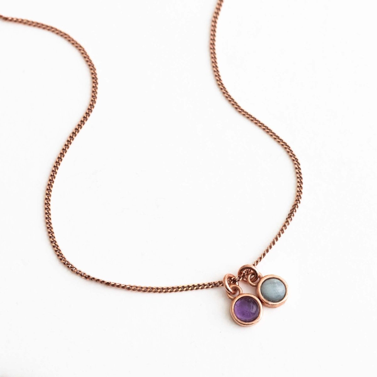 Auf weißem Untergrund liegt eine feine, rosé goldene Panzerkette mit zwei runden Edelstein-Anhängern, einem Amethyst und einem Aquamarin.