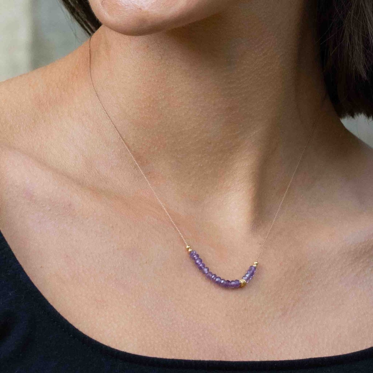 Am Hals des Models hängt eine dünne Seidenkette mit einer Reihe violetter Amethyst-Rondellen und goldenen Zierperlen in der Mitte.
