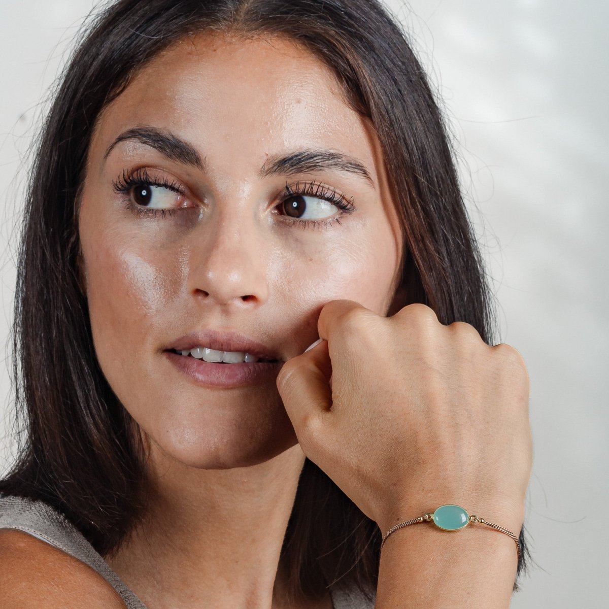 Am Handgelenkt des Models hängt ein feines Seidenarmband mit einem strahlend blauen, ovalen Aqua Chalcedon in der Mitte.