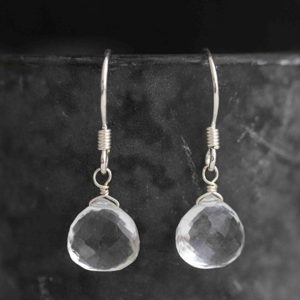 Ein Paar 925 Silber Ohrringe mit bauchigen Bergkristall-Tropfen hängt vor grauem Hintergrund.