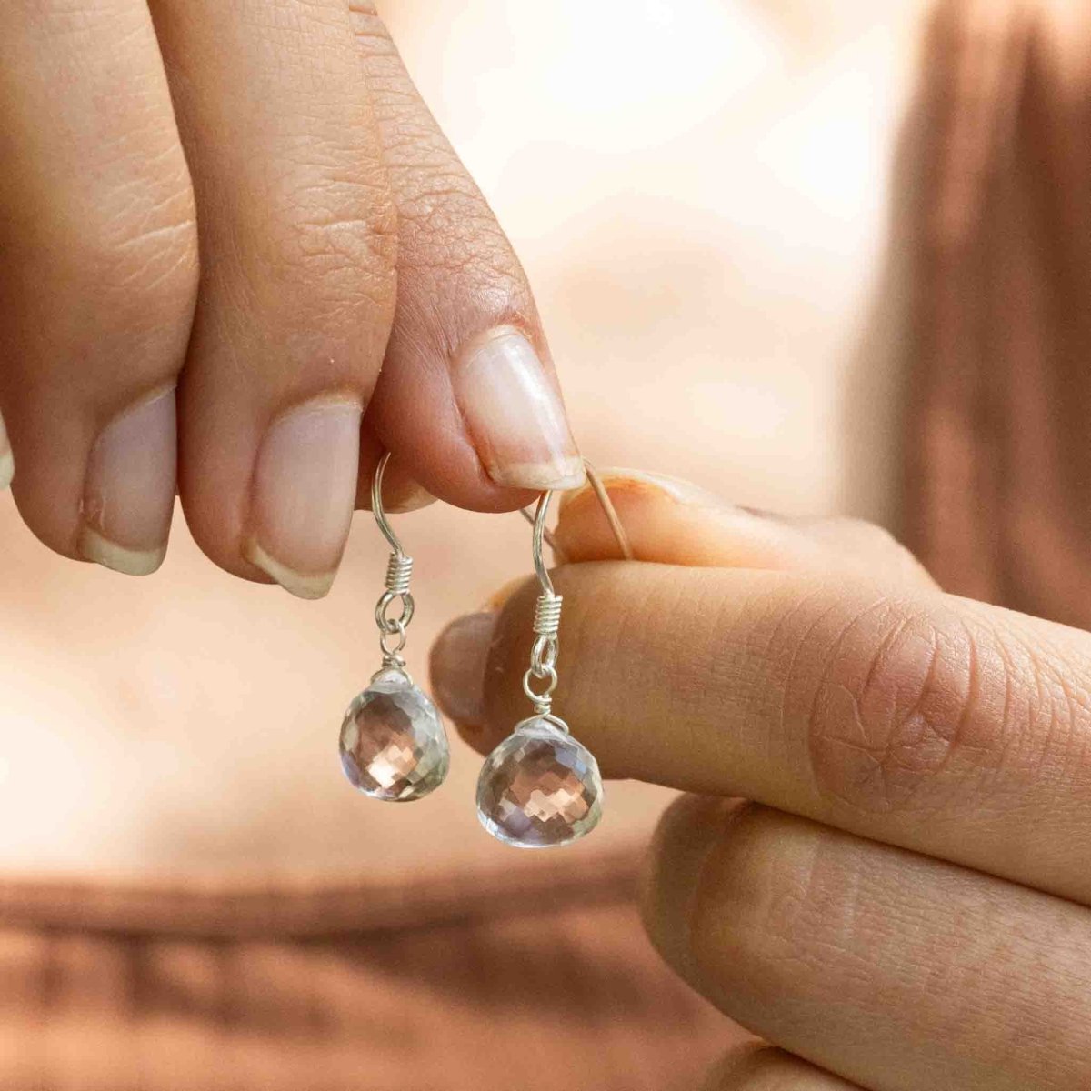 Das Model hält ein Paar silberner Ohrringe mit bauchigen Bergkristall-Tropfen in ihrer Hand.