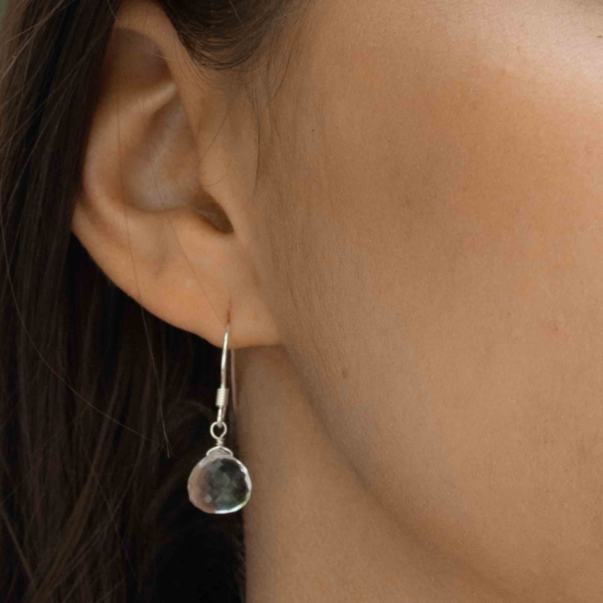 Ein 925 Silber Ohrring, bestehend aus einem einfachen Ohrhaken und einem tropfenförmigen Bergkristall, hängt am Ohr des Models.