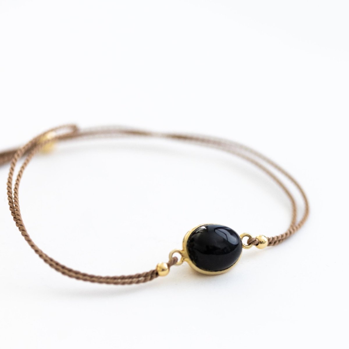 Ein beiges Seidenarmband mit einem Black Star Edelstein in der Mitte auf weißem Hintergrund.