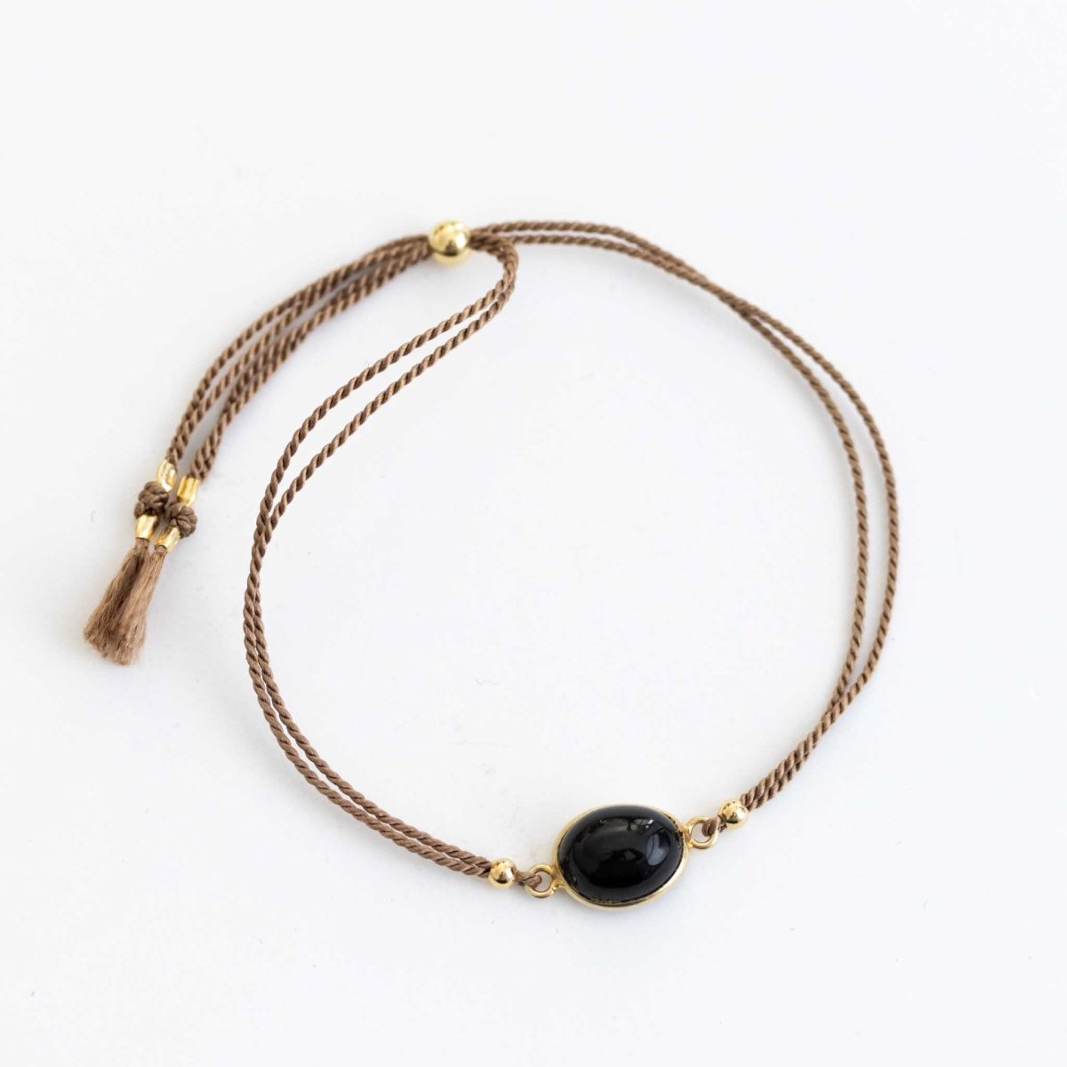 Ein beiges Seidenarmband mit einem Black Star Edelstein in der Mitte auf weißem Hintergrund.