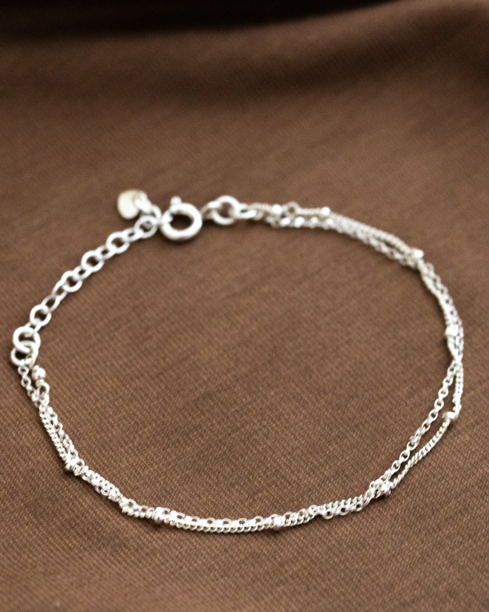 Ein doppelreihiges Silberarmband liegt auf braunem Stoff.