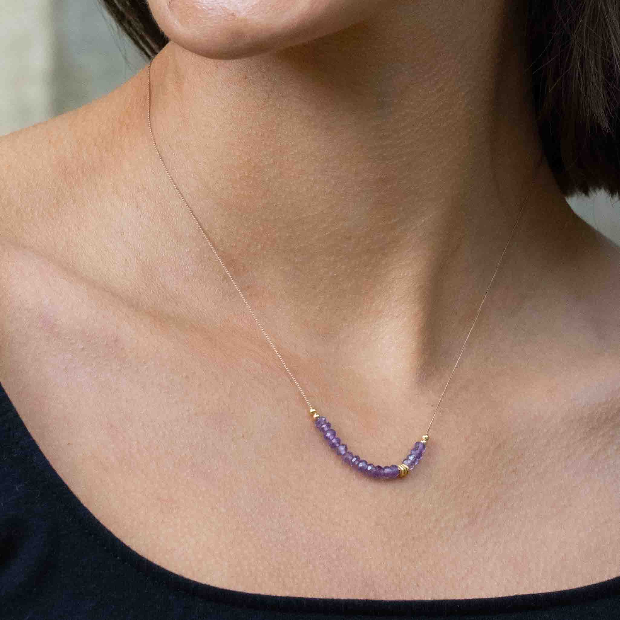 Am Hals des Models hängt eine dünne Seidenkette mit einer Reihe violetter Amethyst-Rondellen und goldener Zierperlen in der Mitte.