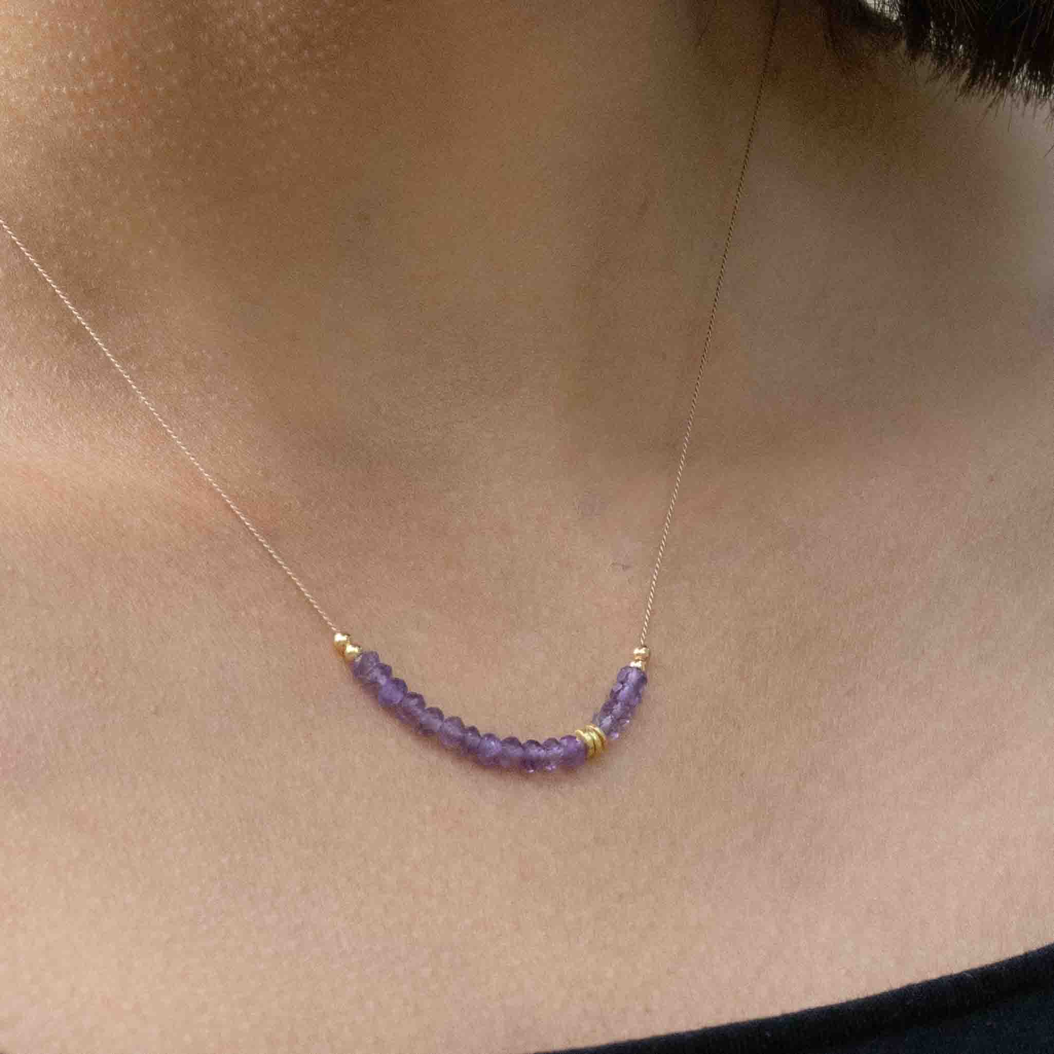 Am Hals des Models hängt eine dünne Seidenkette mit einer Reihe violetter Amethyst-Rondellen und goldener Zierperlen in der Mitte.