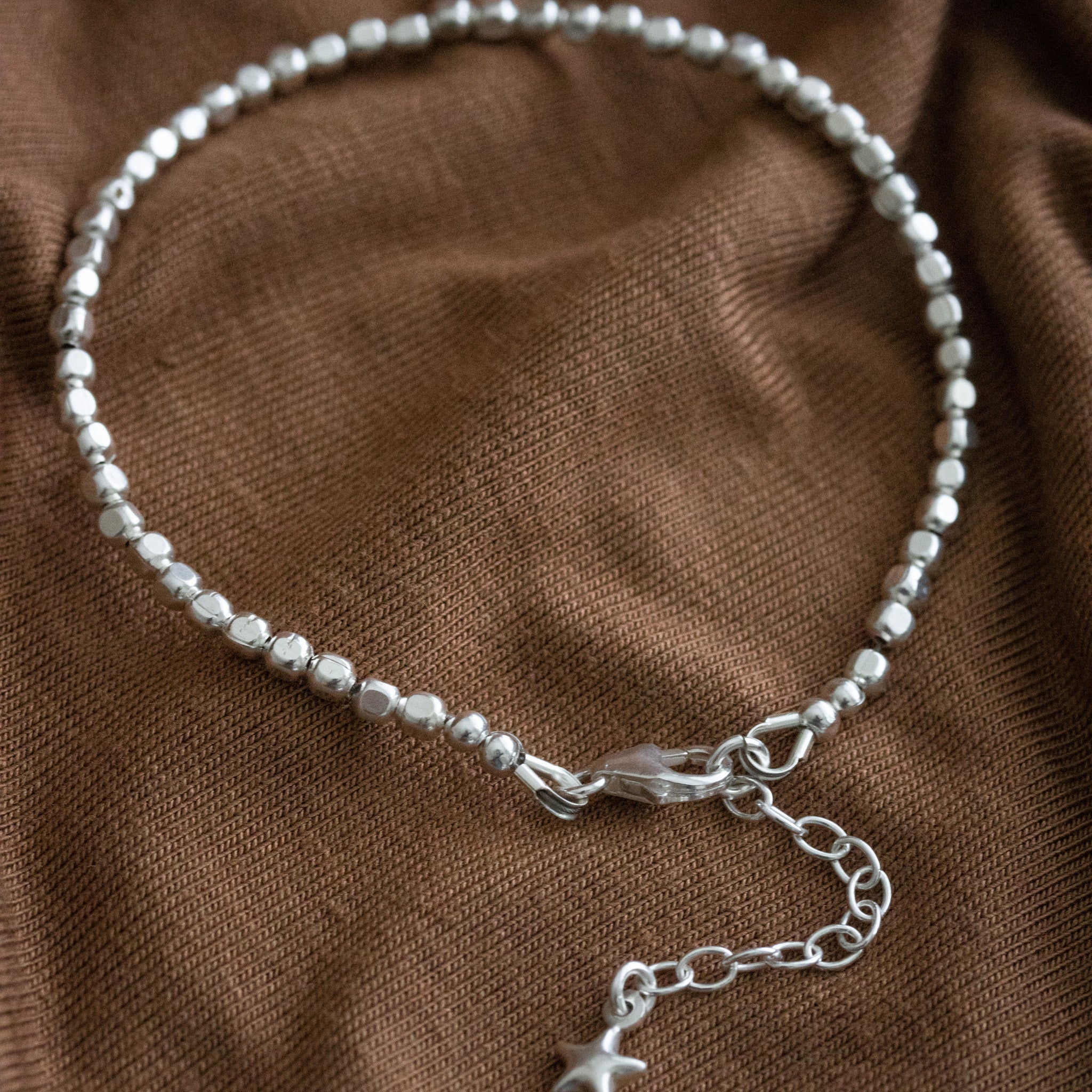 925 Silber Armband aus Mini-Würfeln mit Detail-Ansicht des Karabiner-Verschlusses und Verlängerungskettchen auf Stoff ausgelegt.