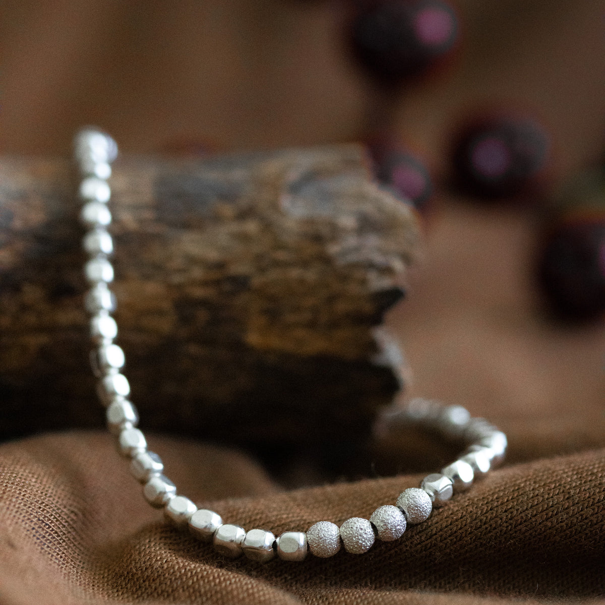 925 Silber Würfel-Armband mit gefrosteten Perlen in der Mitte an ausgelegtem Baumstamm hängend.