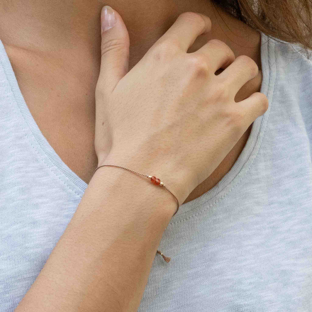 Dünnes Schnurarmband mit orangem Karneol und goldenen Akzenten am Handgelenk getragen.