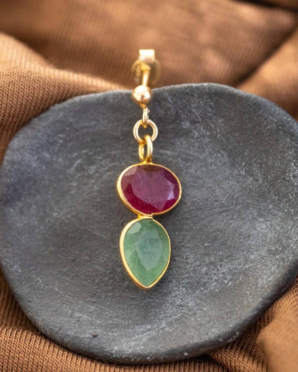 Ein Ohrstecker, der aus einem gold gerahmten Rubin und einem darunter angebrachten, ebenfalls gold gefassten, Prehnit besteht, liegt auf einem dunkelgrauen Steinschälchen.