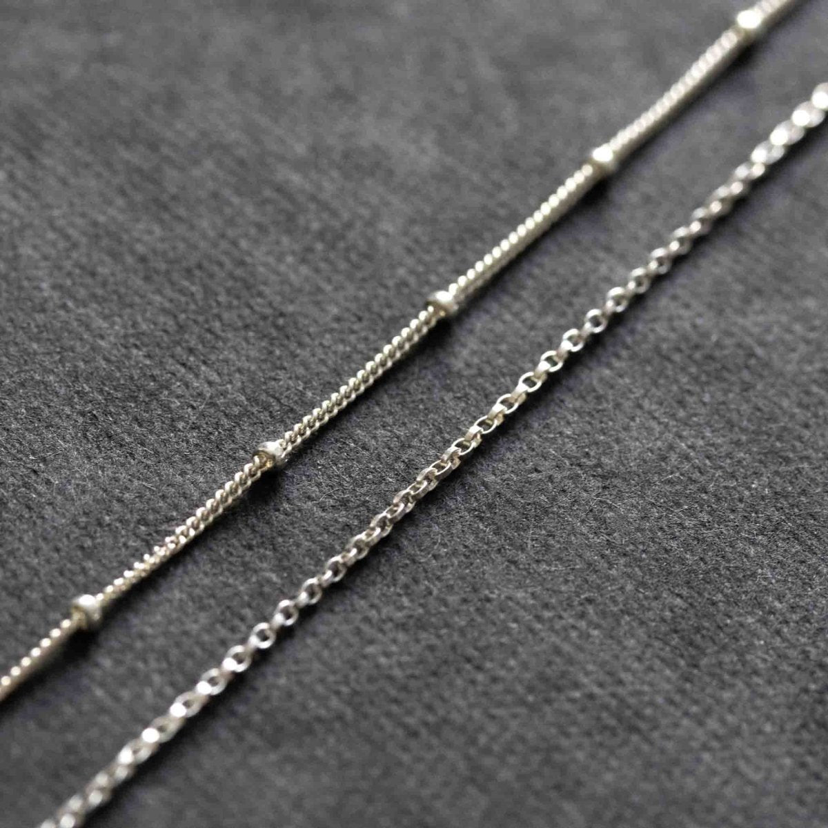 Eine doppelreihige Silberkette, bestehend aus einer Erbskette und einer Satellitenkette, liegt auf einem schwarzen Hintergrund.