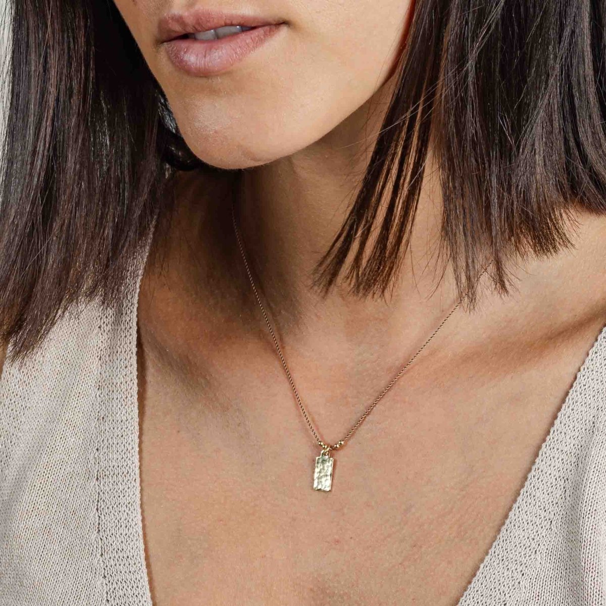 Am Hals des Models hängt eine dünne, beige Seidenkette mit einem rechteckigen Plättchen-Anhänger.