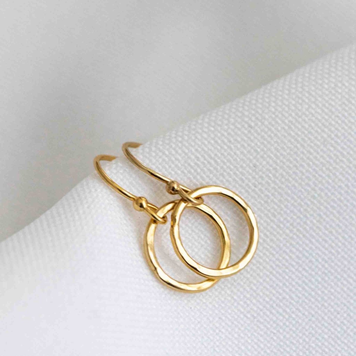 Ein Paar goldener Ohrringe von Mayam Berlin mit Ohrhaken, an denen jeweils ein offener Ring hängt, auf weißem Hintergrund