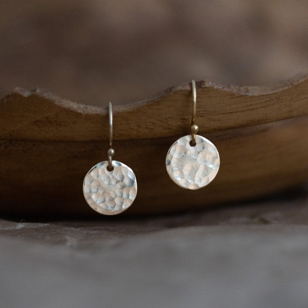 Ein Paar 925 Silber Ohrringe mit gehämmerten, runden Plättchen hängt an einer braunen, gewellten Holzschüssel.