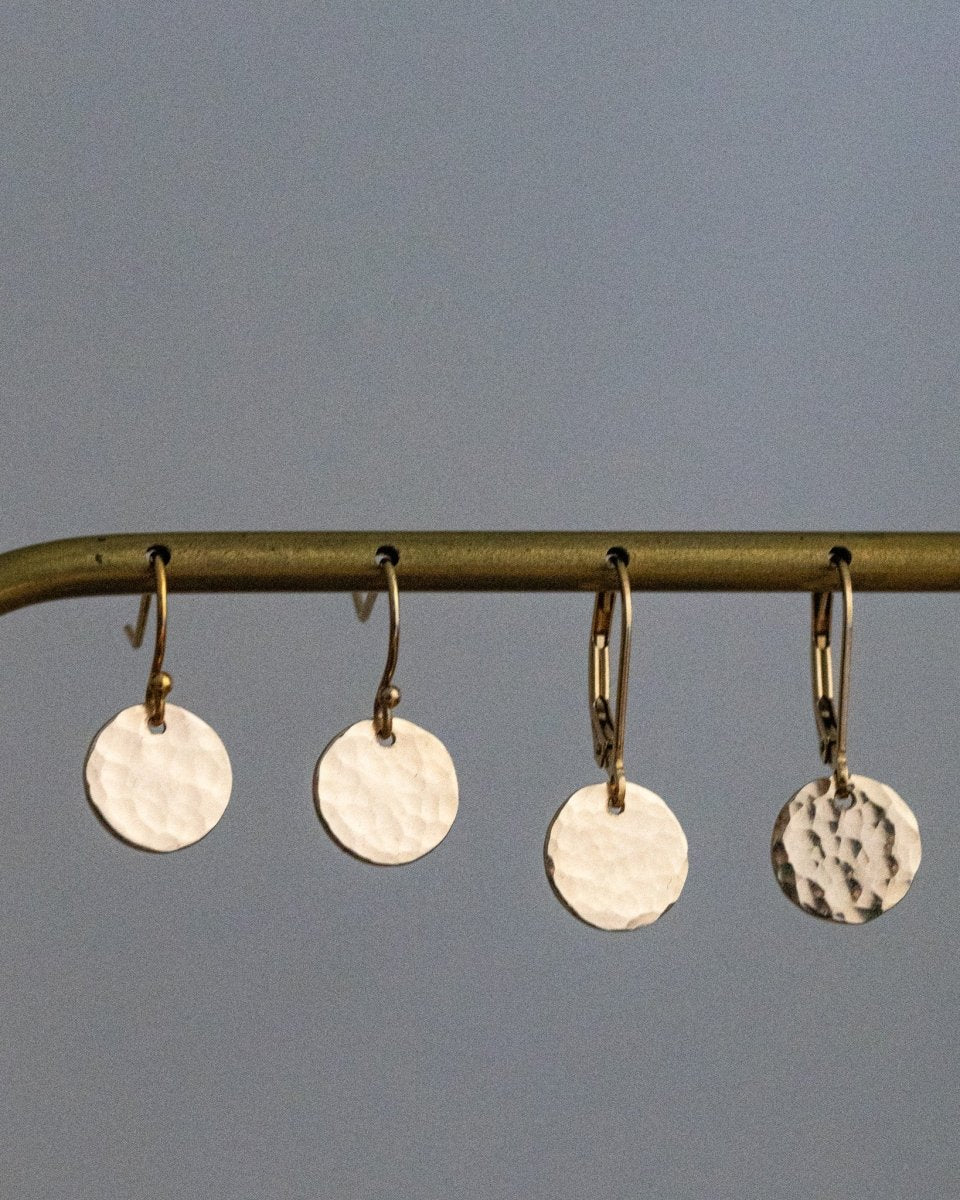 Zwei Paar goldener Plättchen-Ohrringe in Hammerschlag-Optik hängen an einer Messingstange.