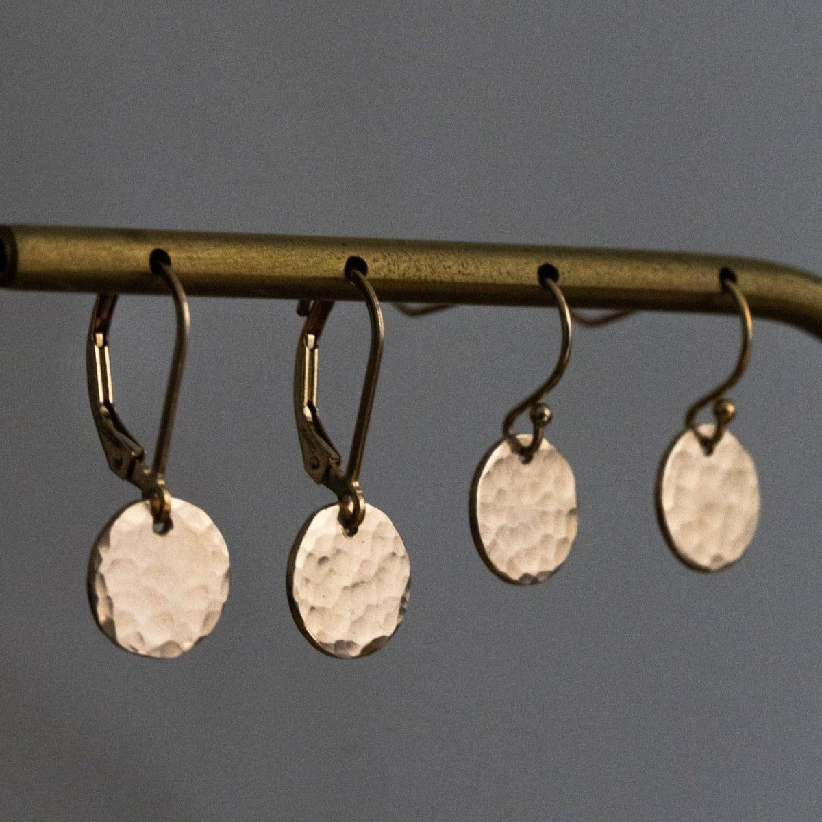 Zwei Paar goldener Plättchen-Ohrringe in Hammerschlag-Optik hängen an einer Messingstange.
