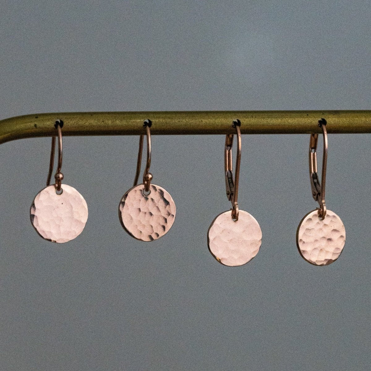 An einer Stange hängen zwei Paar rosé goldener Plättchen-Ohrringe in Hammerschlag-Optik, einmal mit einfachen Ohrhaken und einmal mit Klappbrisur.