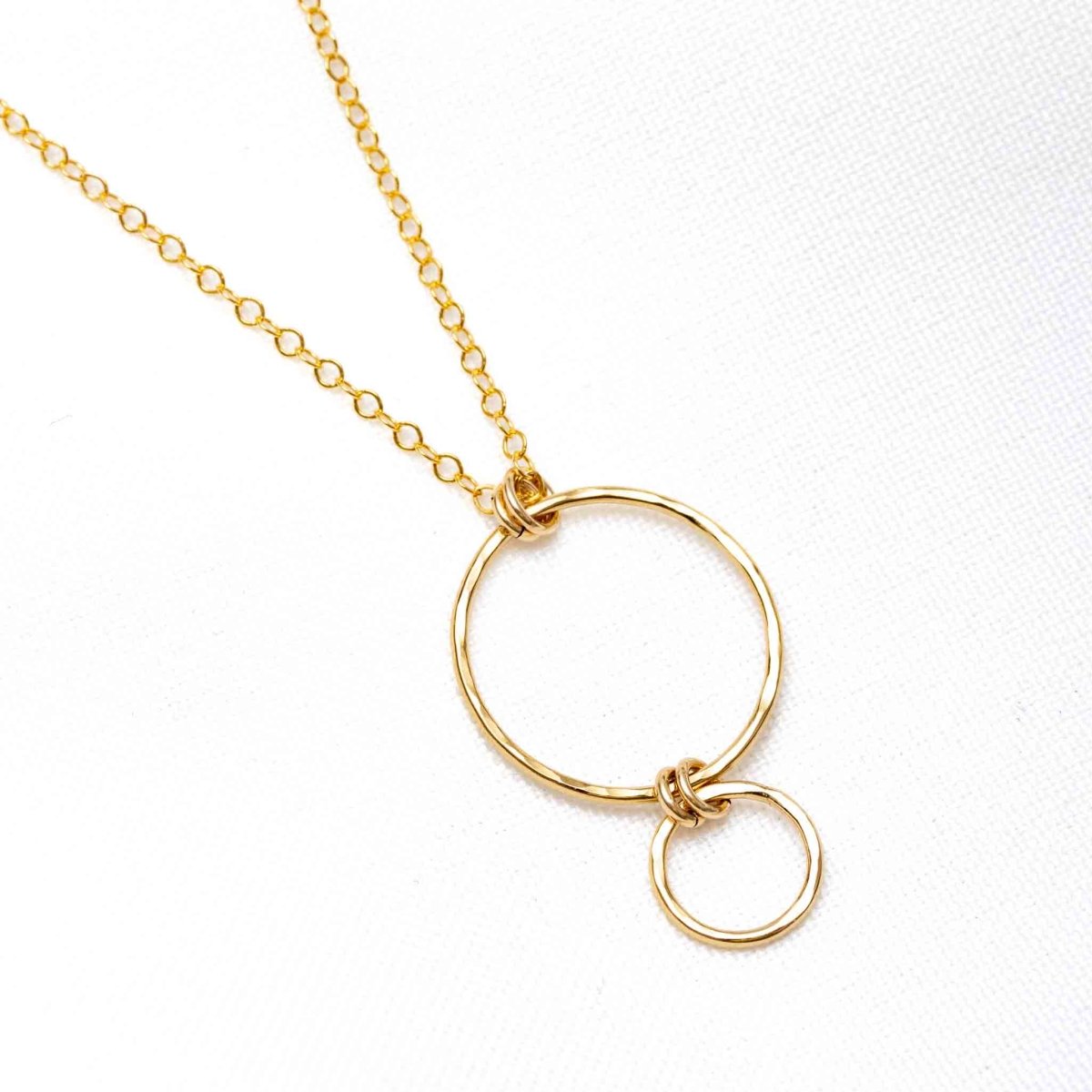 Eine feine Goldkette mit einem Anhänger, bestehend aus einem größeren Ring, an dem ein kleinerer Ring hängt, liegt auf weißem Hintergrund.