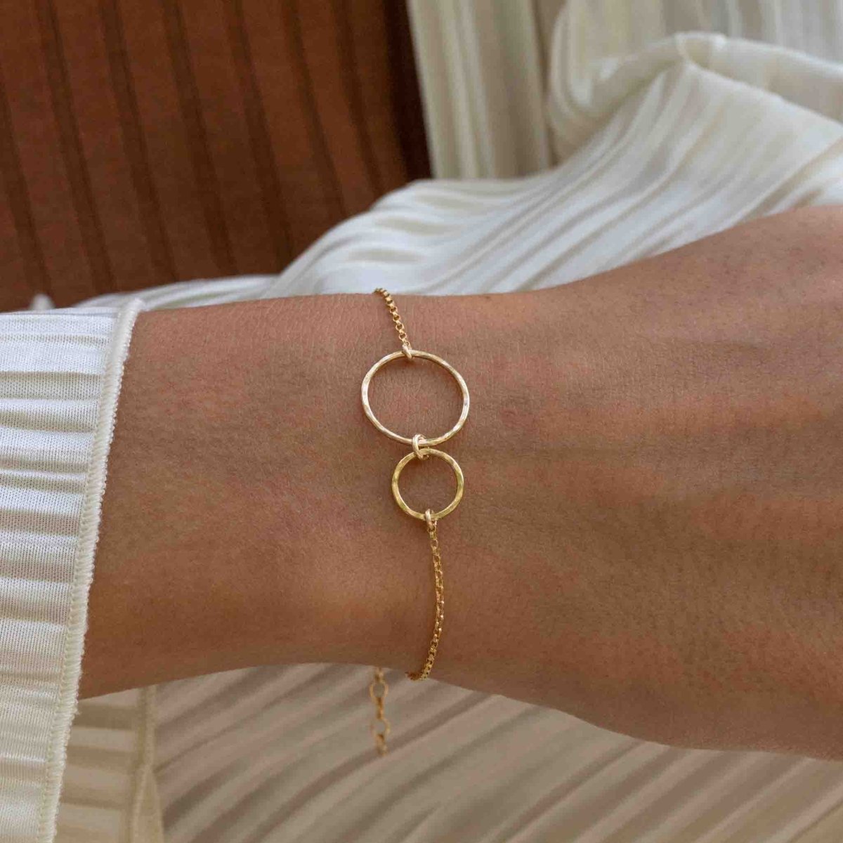 Ein dünnes Goldarmband mit zwei leicht gehämmerten, offenen Ringen am Handgelenk des Models.