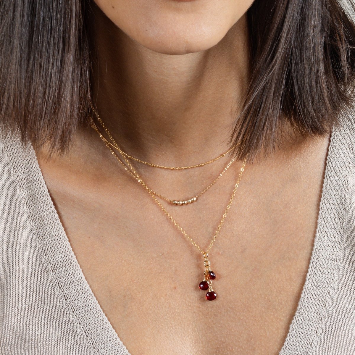 Eine feine Goldkette mit drei untereinander hängenden Granat Edelsteinen hängt zusammen mit zwei kürzeren Goldketten am Hals des Models.