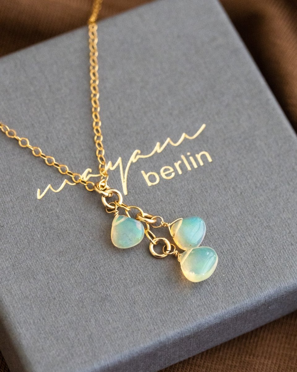 Eine feine Goldkette mit drei Opal-Anhänger liegt auf einem grauen Schmucketui.