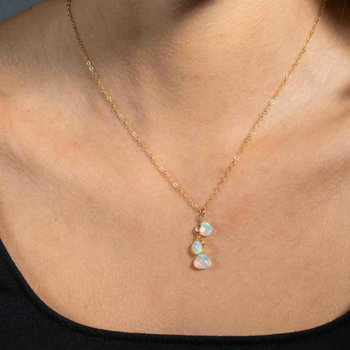 Am Hals des Models hängt eine zarte Goldkette mit drei Opal-Anhängern.