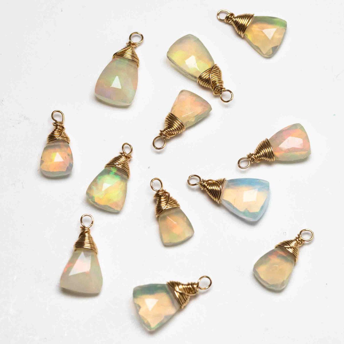 Dreieckige, gold gefasste Opal-Anhänger liegen auf weißem Hintergrund.